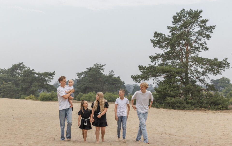 Kinderen spelend en lachend op het zandduin tijdens een fotoshoot.