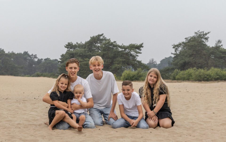Kinderen van familie Wolvering tijdens een spontane fotoshoot op Kootwijkerduin, Apeldoorn, Gelderland, lachend en spelend tijdens creatieve opdrachtjes.