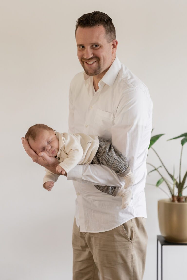 Slapende baby op arm van papa tijdens newbornshoot aan huis in Voorthuizen